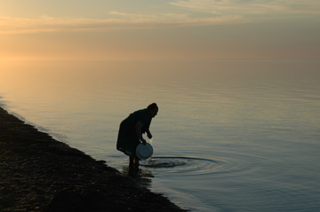 Photograph of woman wahsing plate at edge of lake at sunset